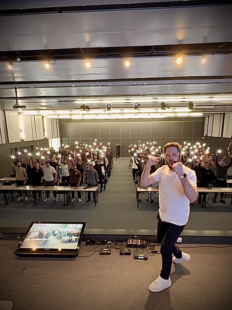 Claiton Costa no palco de uma aula, com o público ao fundo